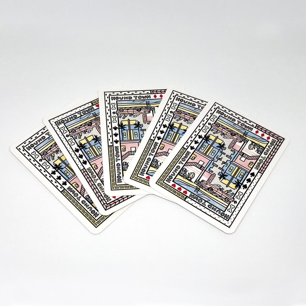 Five Clare Duffy artist playing cards fanned out showing the artwork on the back of all cards which features an artwork that can be viewed both directions, it features a Hound Town scene including a hotel and a motel with a chevy and a pool, palm trees and dogs and has borders with bones and various patterns.