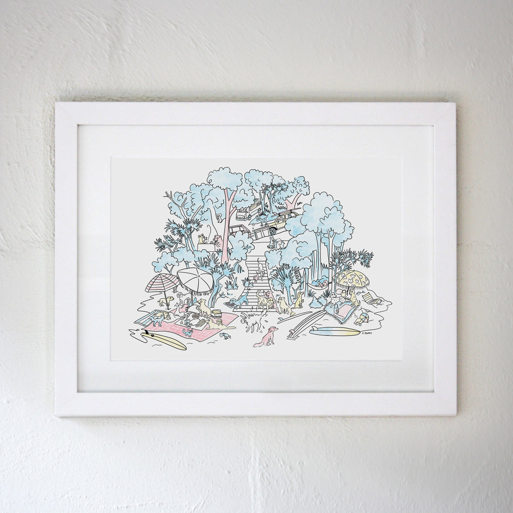 A white frame on a white wall featuring a Clare Duffy Hound Town illustration of a dog picnic scene in which cartoon surf dogs sit amongst the Australian beach destination The Pass in Byron Bay