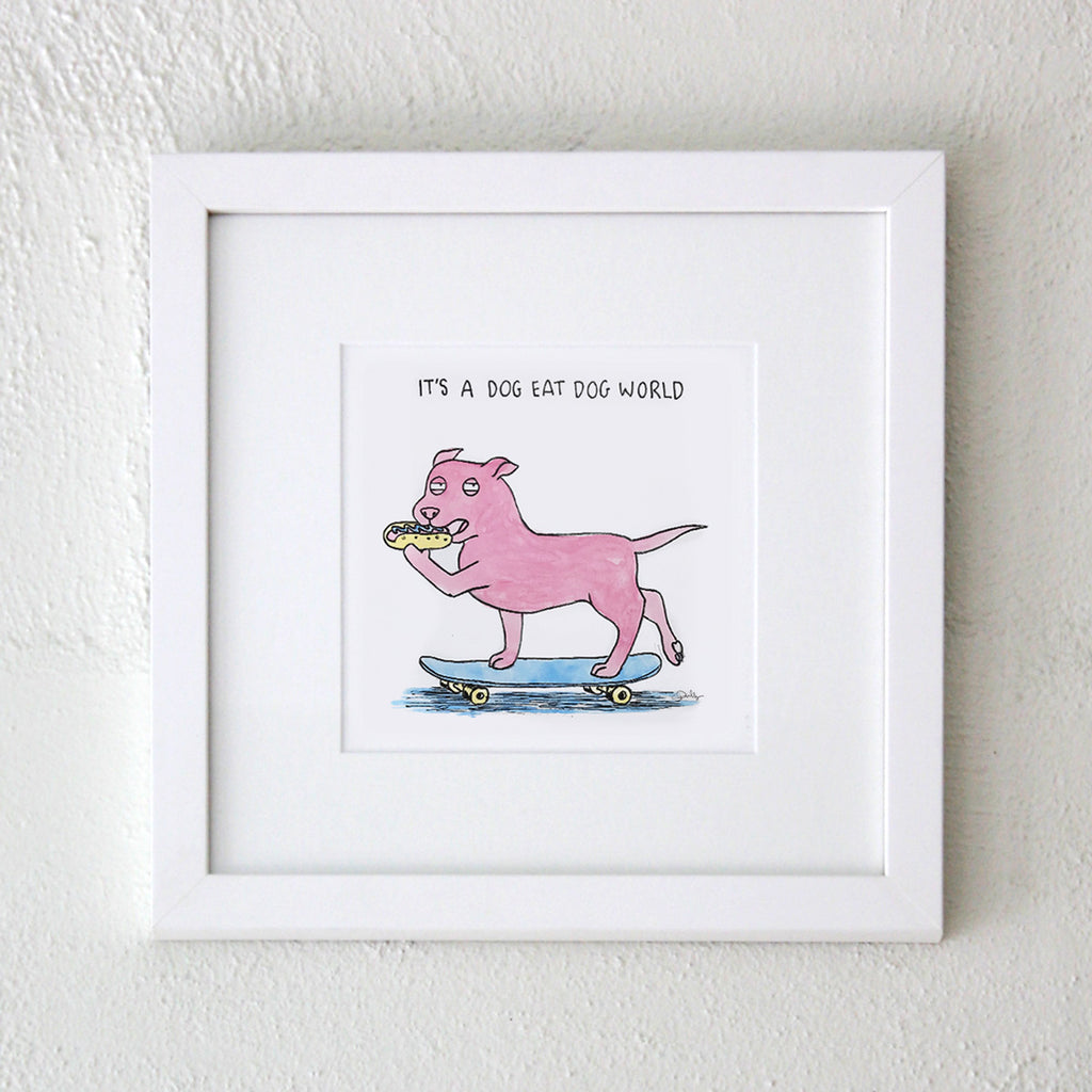A white frame featuring a watercolour print of a dog on a skateboard about to bite into a hotdog with a suspicious expression and the words above read "it's a dog eat dog world" the frame sits on a white textured wall artwork is by Clare Duffy for Hound Town