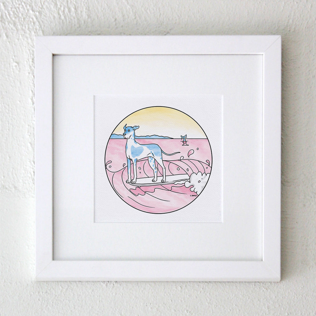 A white framed artwork with wide matt featuring A Hound Town fine art print on a light blue background featuring a great dane with blue patches surfing and hanging ten on a pink wave inside a circle - artwork by Clare Duffy