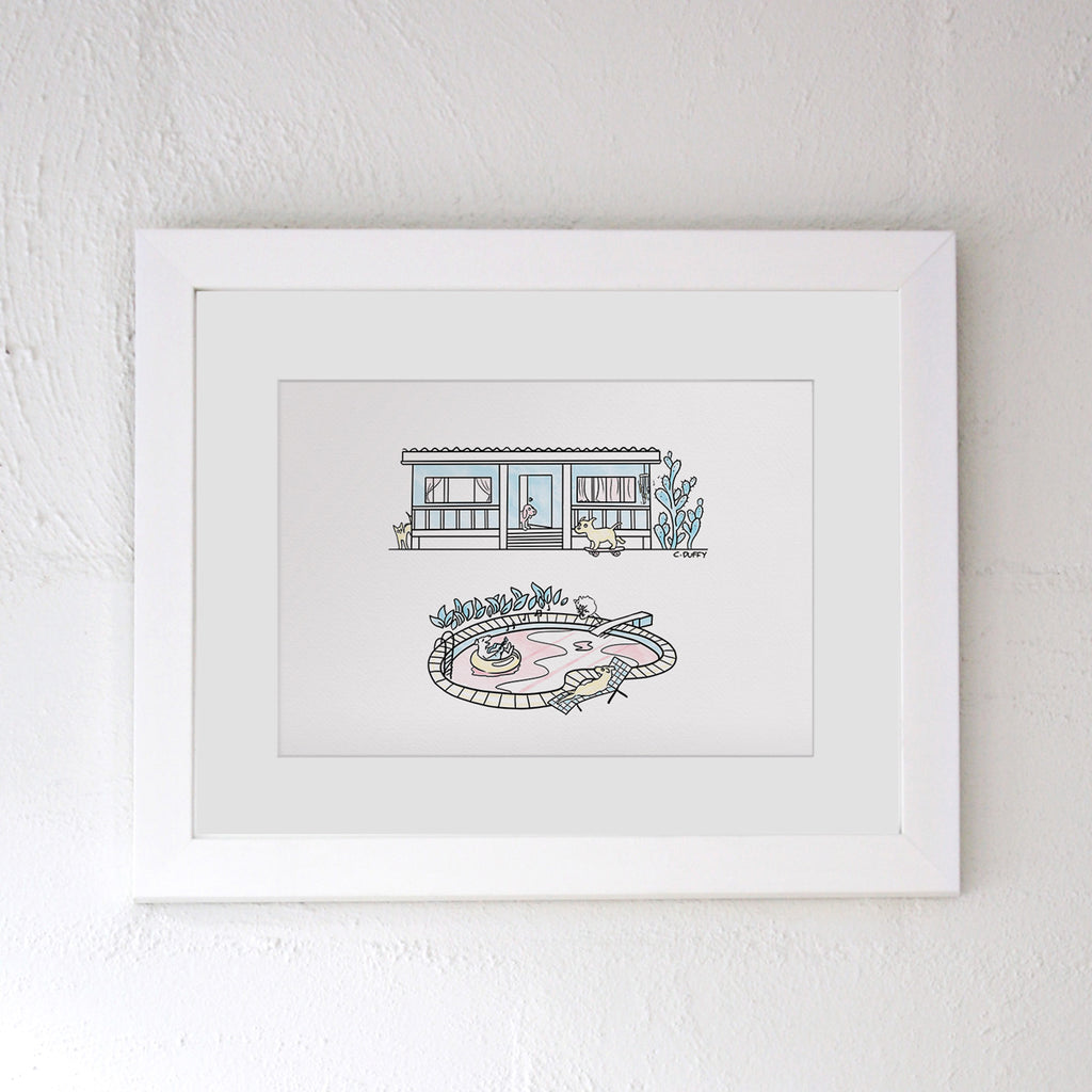 A framed Hound Town print landscape format - the artwork features a fishermans cottage with a cartoon dog skating past, a cactus and a cat, and in front there is a pool with a dog jumping from the diing board, a labrador singing with a guitar and a kelpie on a deck chair
